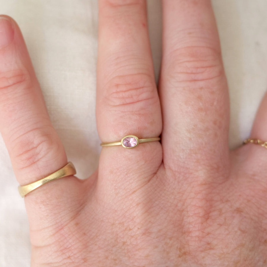 Hand wearing two gold rings with a pink gemstone on a white background