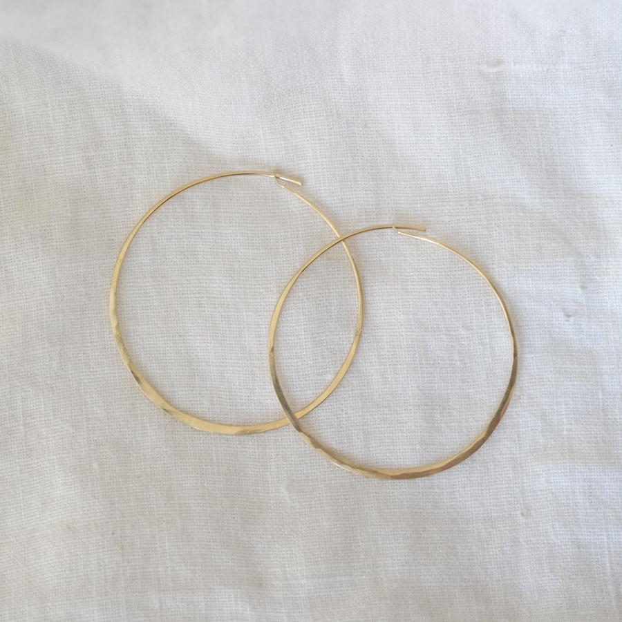 Two gold hoop earrings on a white fabric background