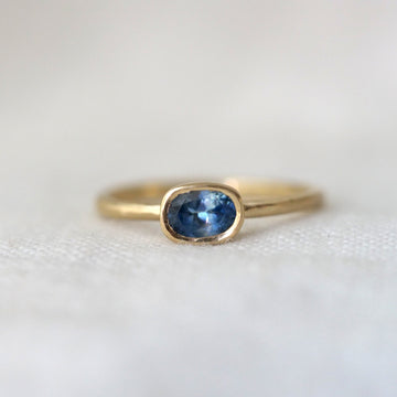 Gold ring with an oval blue gemstone on a white background