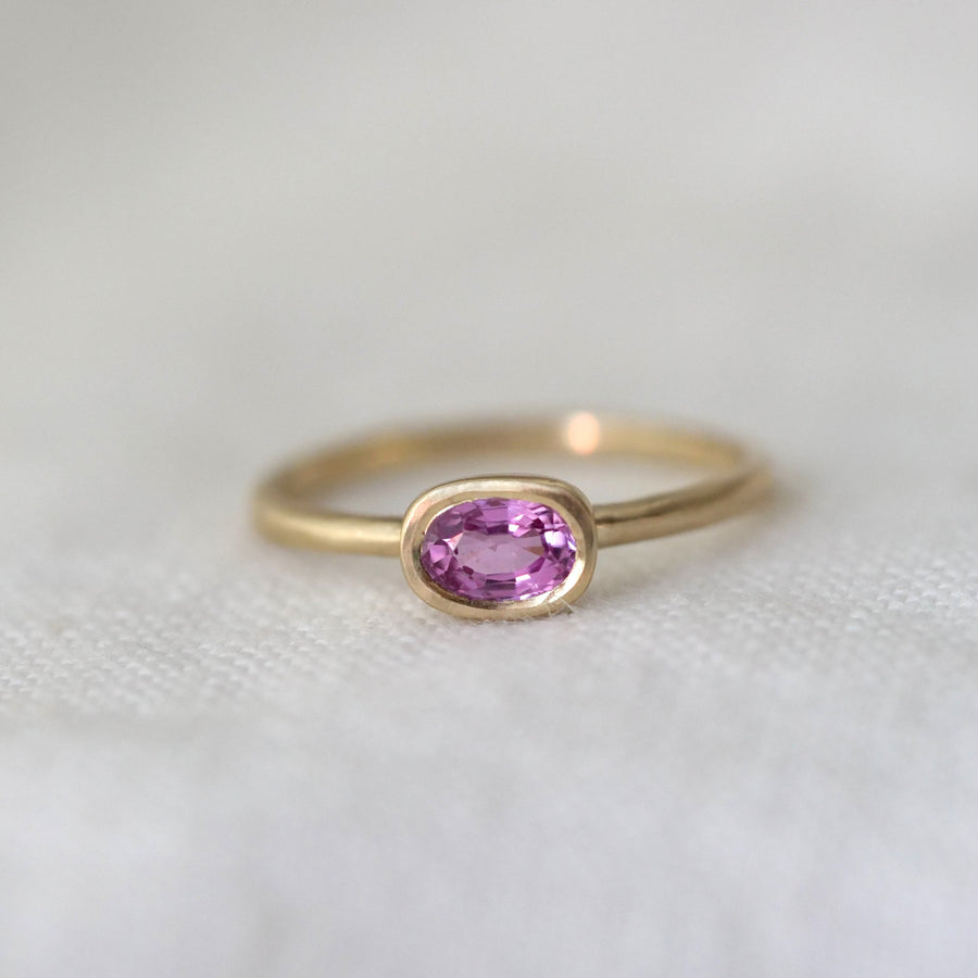 Gold ring with a pink gemstone on a white fabric background