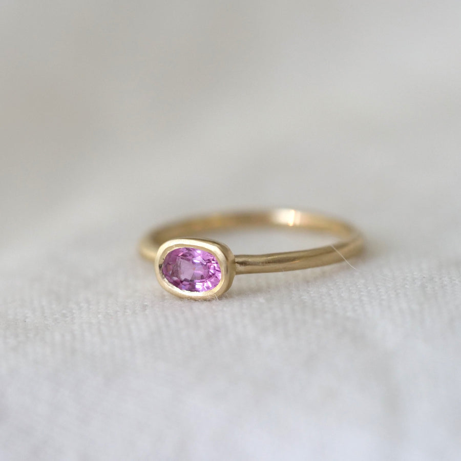Gold ring with a pink gemstone on a white fabric background