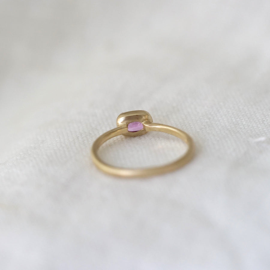 Gold ring with a pink gemstone on a white fabric background