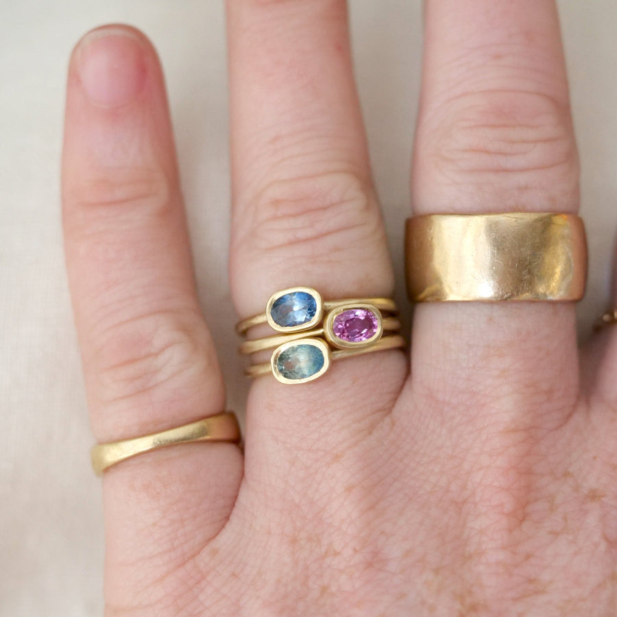 Hand wearing multiple gold rings with gemstones on a neutral background
