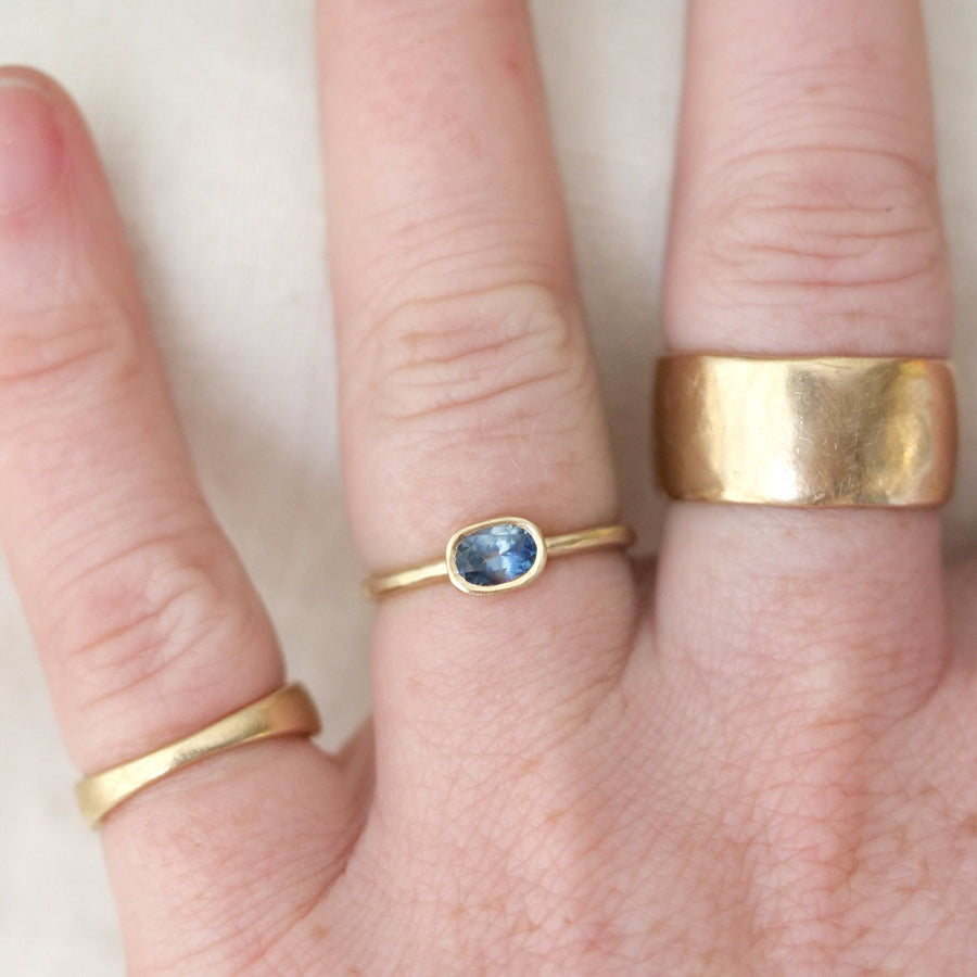 Close-up of a hand wearing multiple gold rings with a blue gemstone on a light background