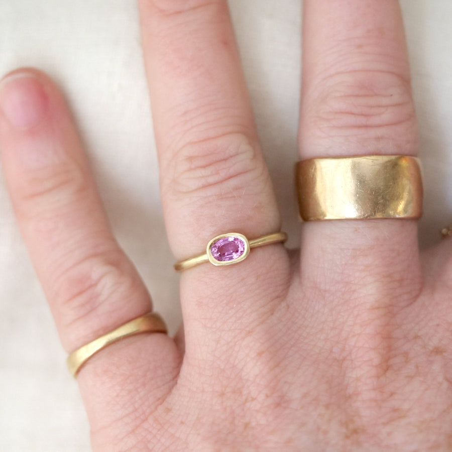 Hand wearing multiple gold rings with a pink gemstone on a light background