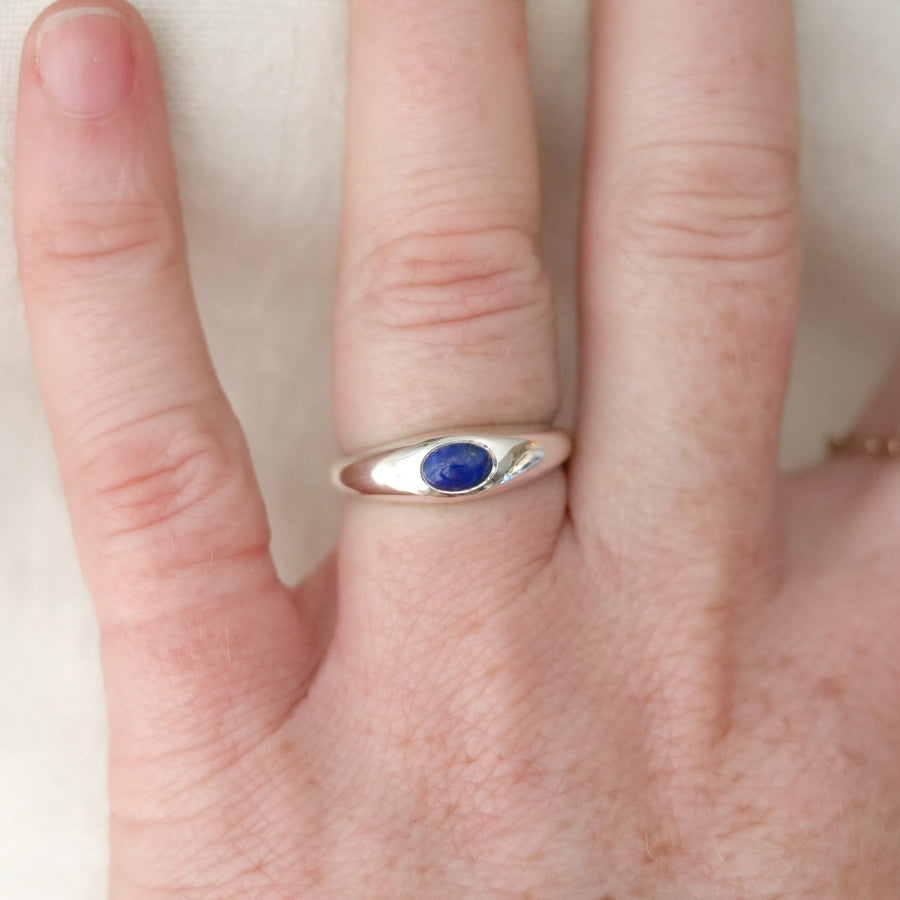 Silver ring with a blue stone on a person's finger against a neutral background