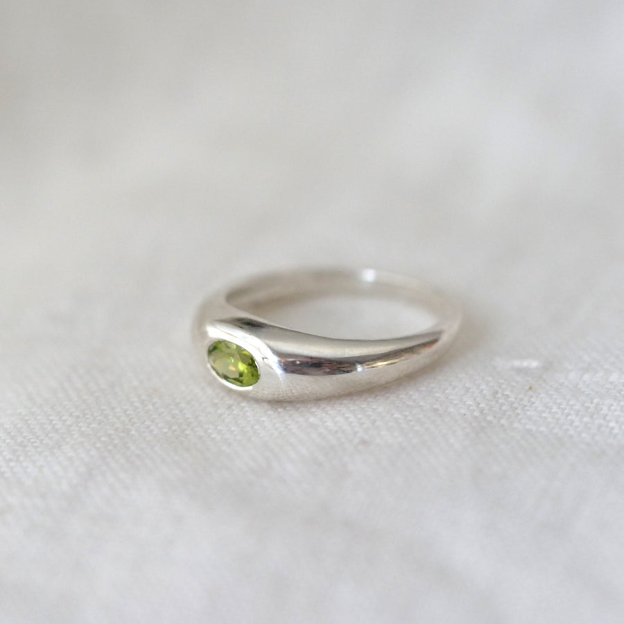 Silver ring with a green gemstone on a white fabric background