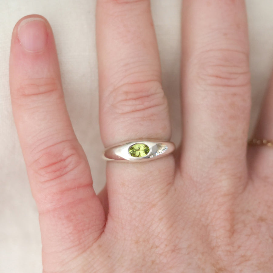 Hand wearing a silver ring with a green gemstone on a plain background