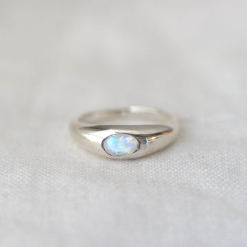 Silver ring with a central multicolor gemstone on a light gray background