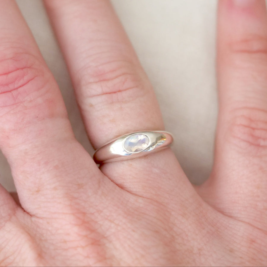 Hand wearing a gold ring with a clear stone on a plain background