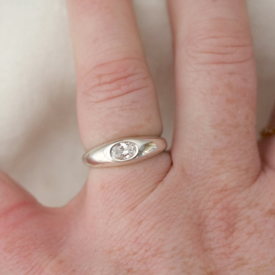 Close-up of a hand wearing a silver ring with a diamond on a light background