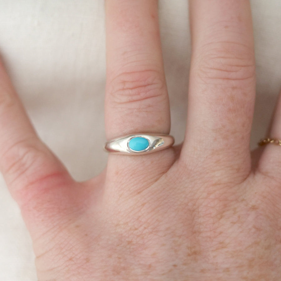 Hand wearing a silver ring with a turquoise stone on a white background