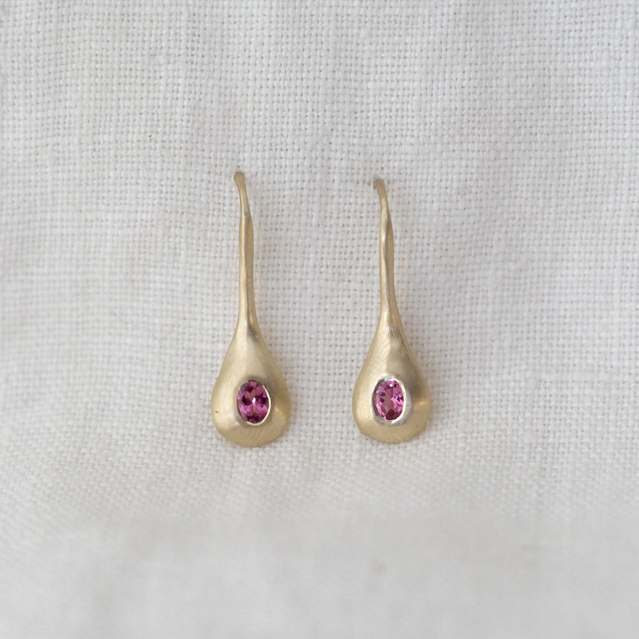 Gold earrings with pink gemstones on a light gray background