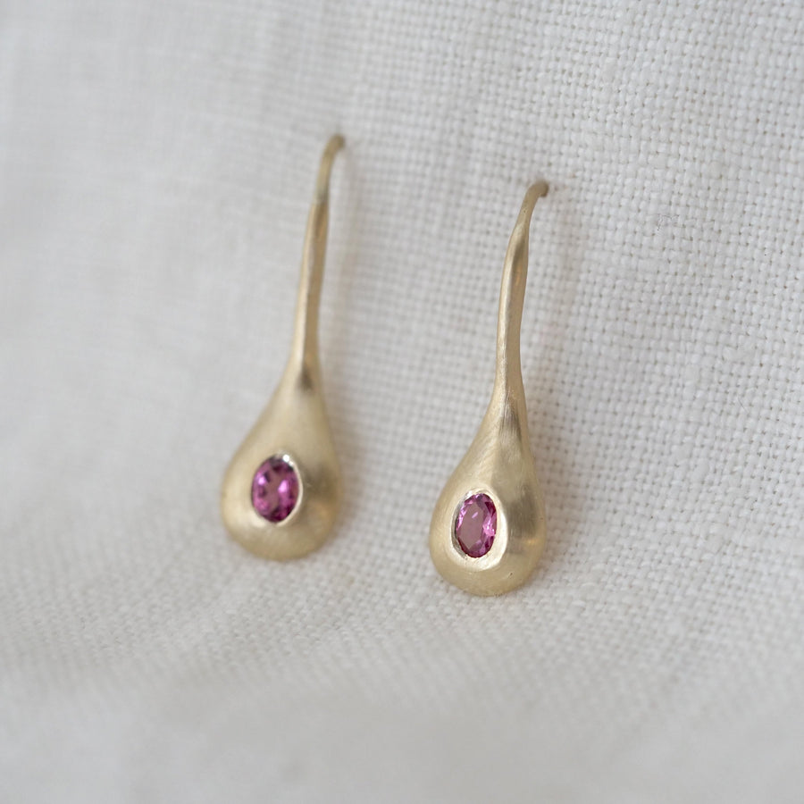 Gold teardrop-shaped earrings with pink gemstones on a light gray background
