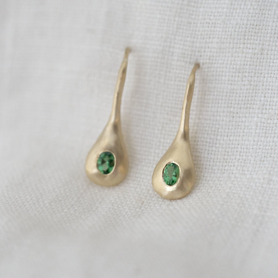 Gold teardrop earrings with green gemstones on a white fabric background