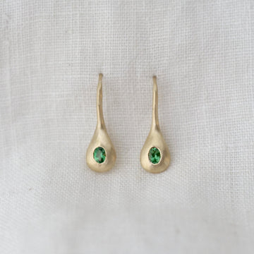 Gold earrings with green gemstones on a light gray fabric background