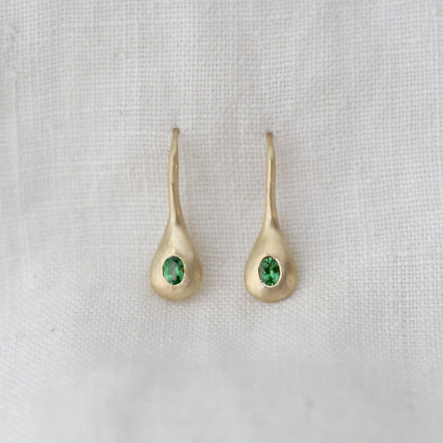 Gold earrings with green gemstones on a light gray fabric background