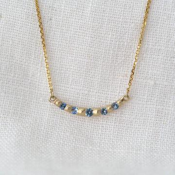 Gold necklace with blue stones on a white fabric background