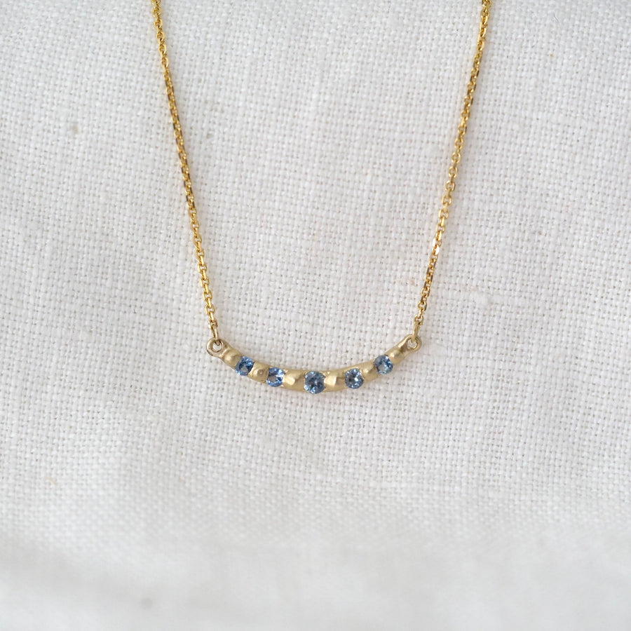 Gold necklace with small blue stones on a white fabric background