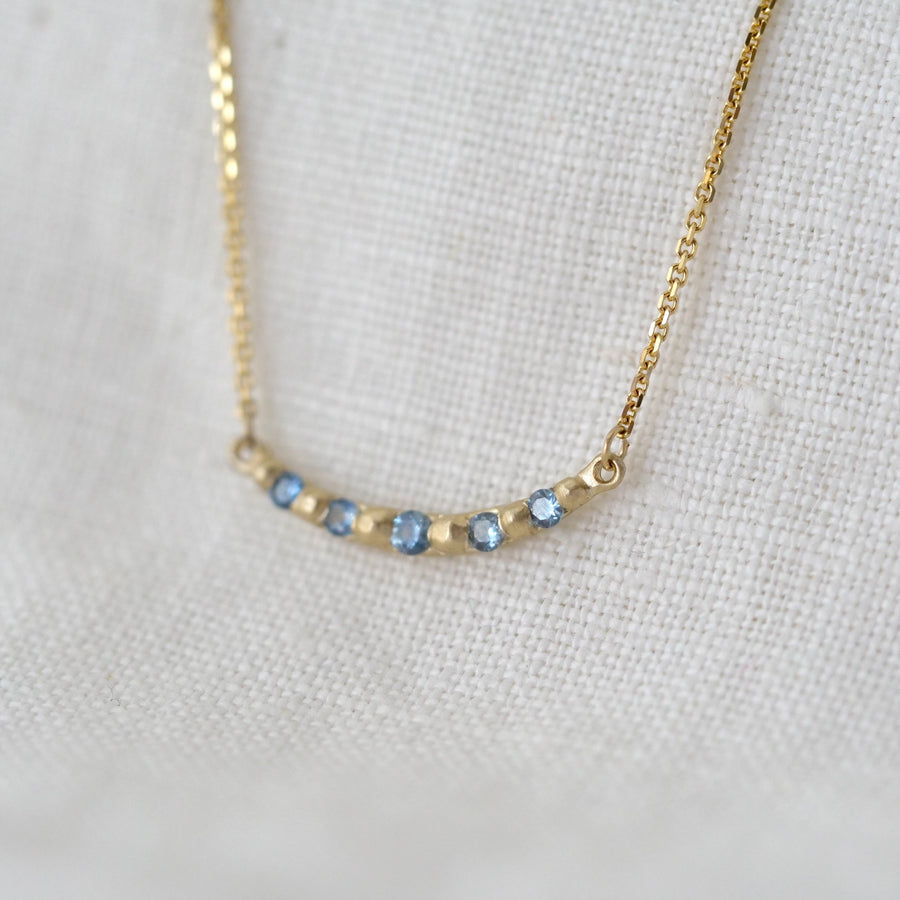 Gold necklace with small blue stones on a light gray background
