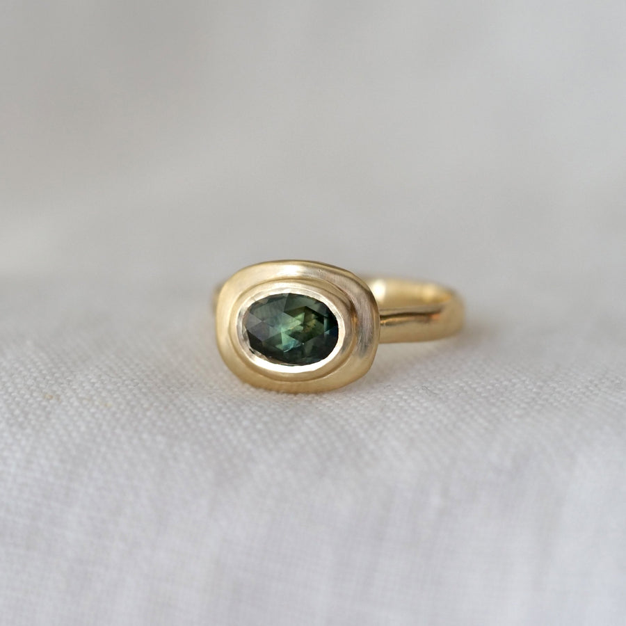 Gold ring with a green gemstone on a white fabric background