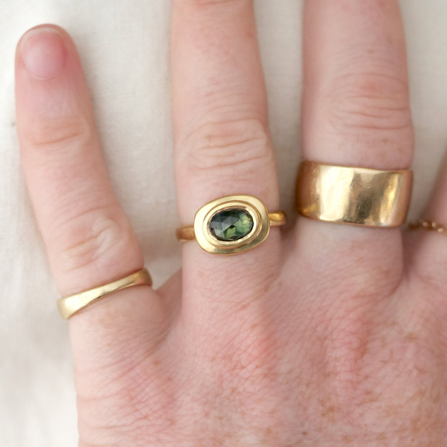 Hand wearing three gold rings with a green gemstone on a white background