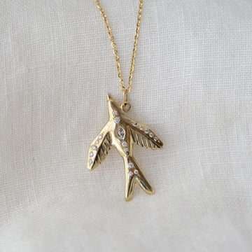 Gold bird-shaped pendant necklace with diamonds on a light gray background