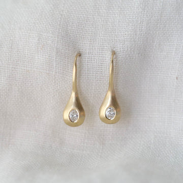Gold teardrop earrings with clear stones on a light fabric background