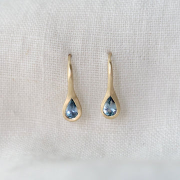Pair of gold teardrop earrings with light blue gemstones on a white fabric background
