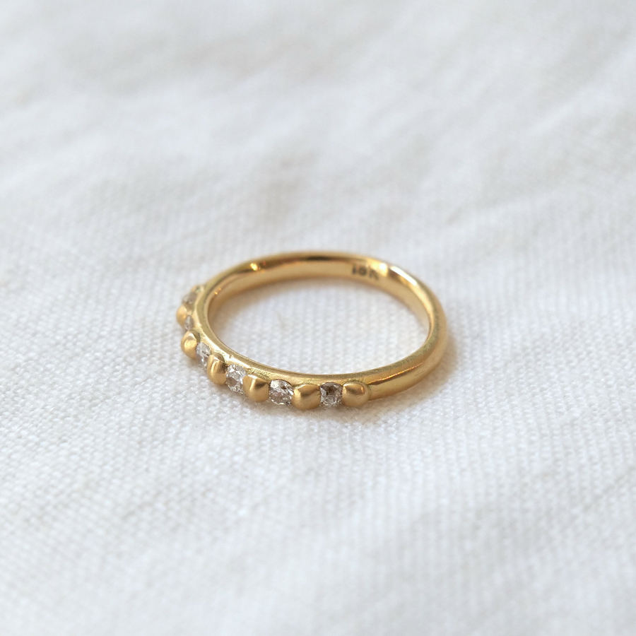 A golden ring with small Cora Classic - Antique Diamonds set symmetrically around it, resting on a plain white fabric background. The setting shows subtle elegance by Marisa Mason Jewelry.
