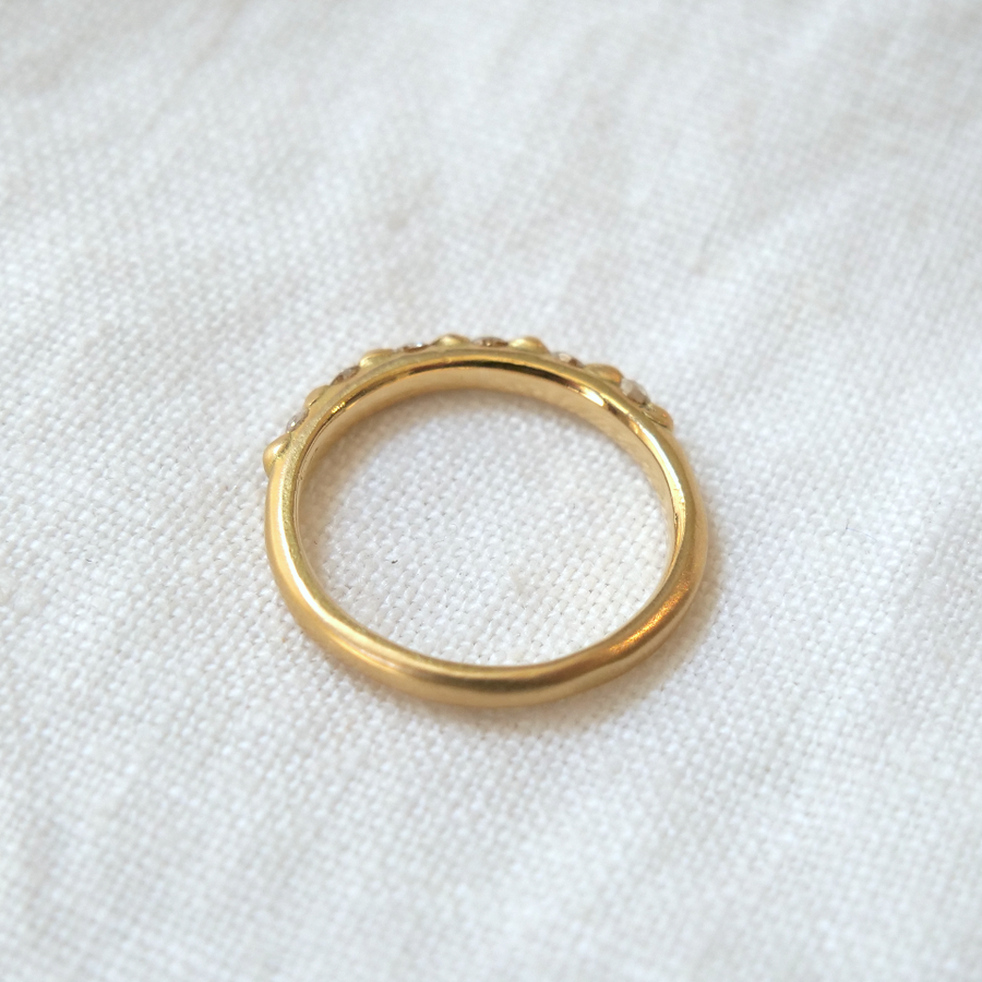 A gold ring with a scalloped design featuring Cora Classic - Antique Diamonds rests on a white textured fabric, emphasizing simplicity and elegance by Marisa Mason Jewelry.