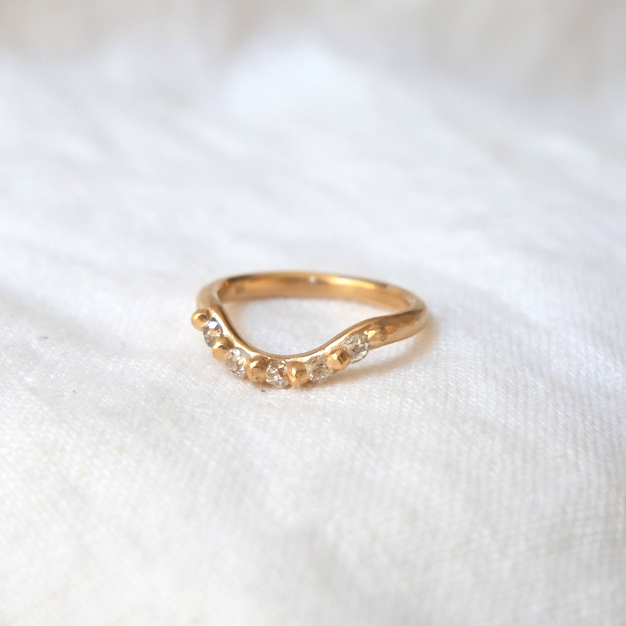 Rounded gold band with carved gold granulation details used to set five diamonds stones, creating a curve in the band that makes room for wearing with a solitaire ring