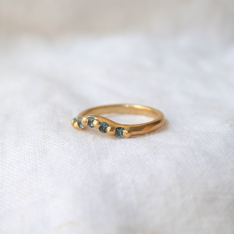 Rounded gold band with carved gold granulation details used to set five montana sapphires stones, creating a curve in the band that makes room for wearing with a solitaire ring