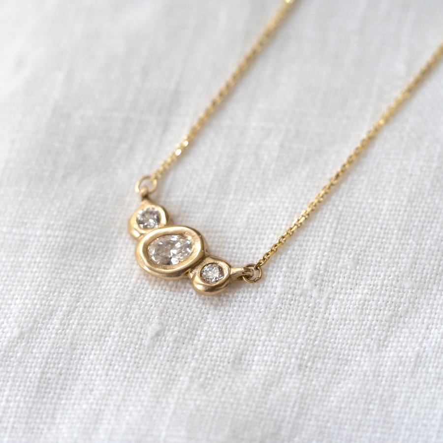 Organically sculpted 3 stone necklace, with one larger oval cut diamond and 2 small round diamonds on either side, bezel set in 14k yellow gold.  Marisa Mason Jewelry