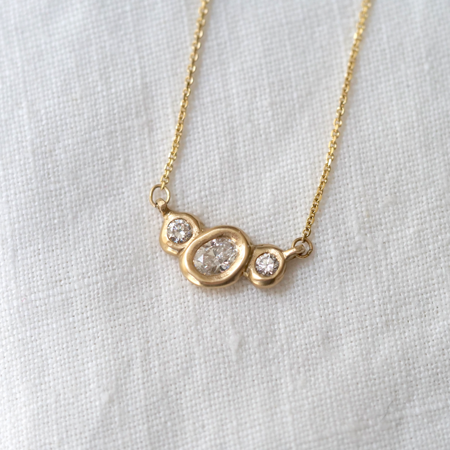 Organically sculpted 3 stone necklace, with one larger oval cut diamond and 2 small round diamonds on either side, bezel set in 14k yellow gold.  Marisa Mason Jewelry