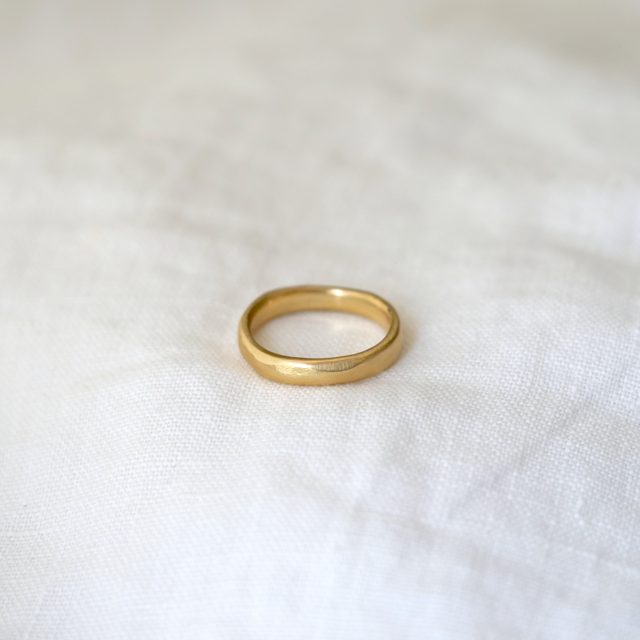 A classic gold band but with a much more organic look through uneven edges, dimpled texture surface, and a general 