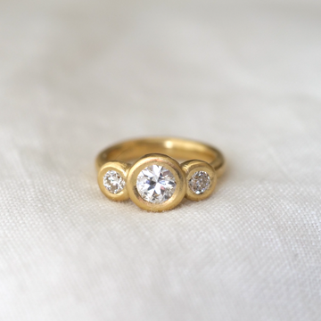 Three white diamonds bezel set in 18k yellow gold, center stone being large and the side stones being smaller