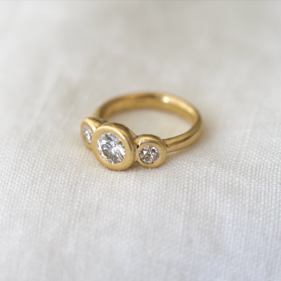 Three white diamonds bezel set in 18k yellow gold, center stone being large and the side stones being smaller