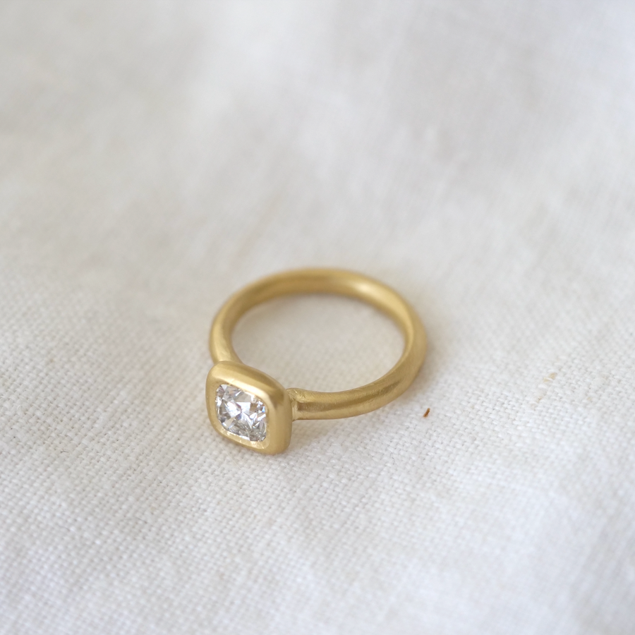 cushion cut diamond is bezel set in luxurious 18k gold