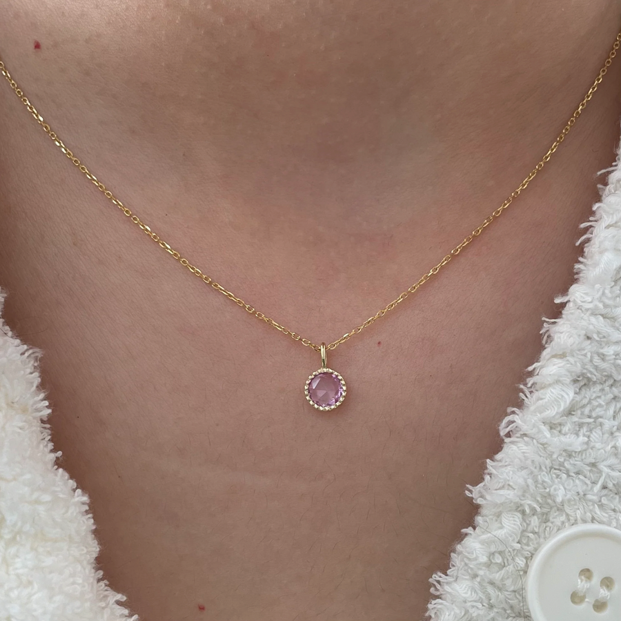 A sweet pink sapphire sits in a milgrain setting on an 18 inch 14k gold chain on model