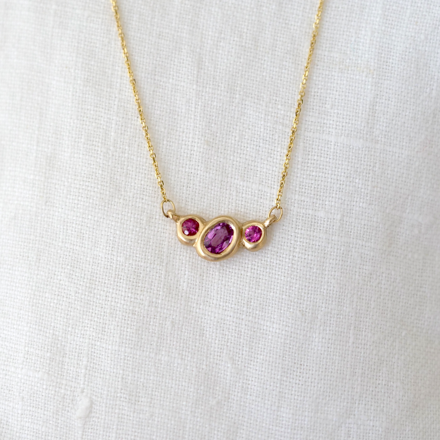 Organically sculpted 3 stone necklace, with one larger oval sapphire and 2 small round tourmaline on either side, bezel set in 14k yellow gold