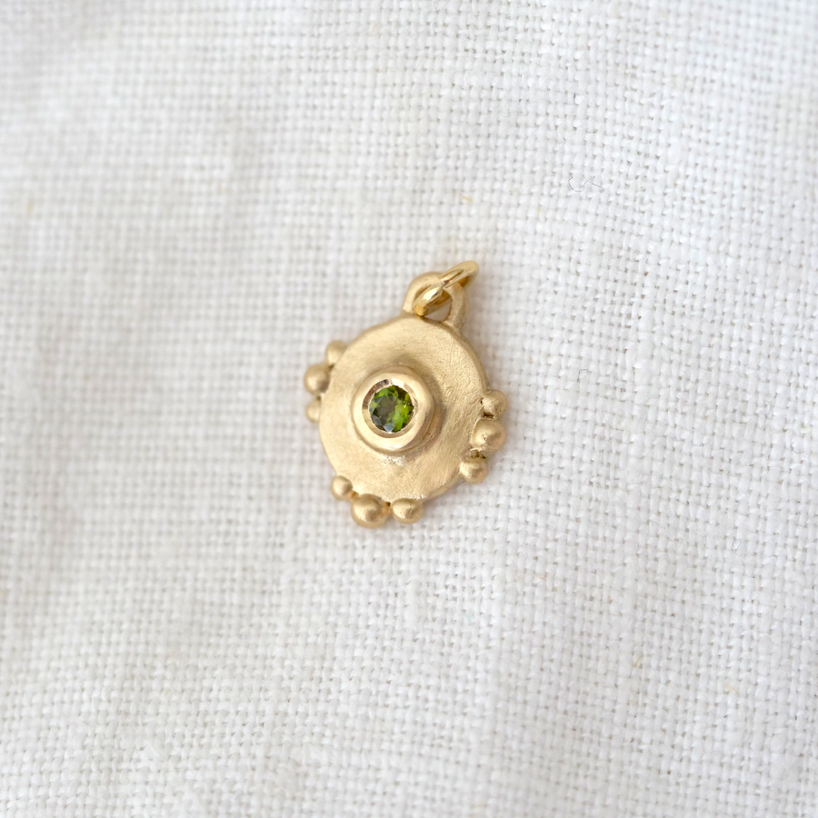 pendant is round with small granulation details on the top, bottom and sides, and bezel set with a light green tourmaline