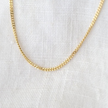 A gold curb chain necklace laid out on a textured fabric surface.