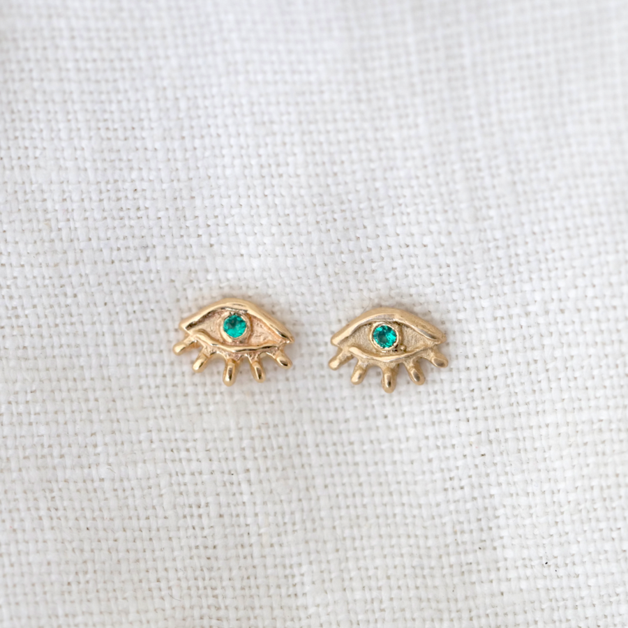 14k eye shaped stud earrings with Little bitty lashes rim the lower half, while the set emeralds acts a pupil