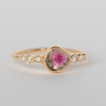 Organically shaped watermelon tourmaline that is green on the edge and pink in the center. Bezel set on a tink gold band with three round white diamonds bezel set on either side