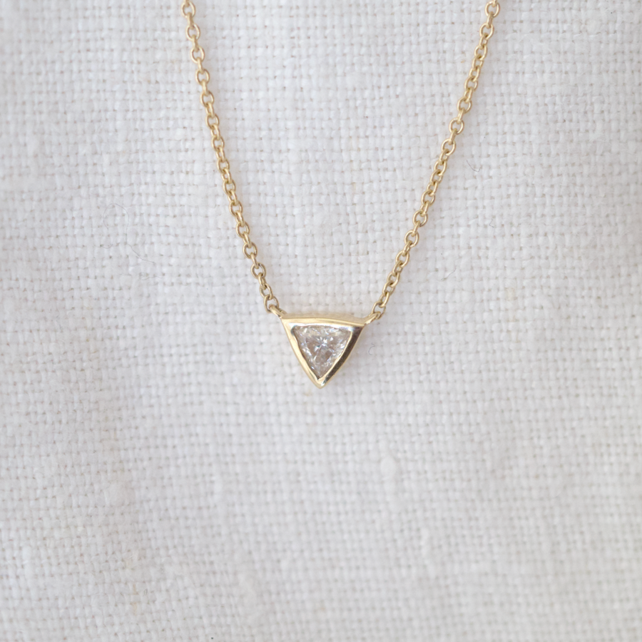 This delicate gold chain features a bezel set trillion cut diamond solitaire