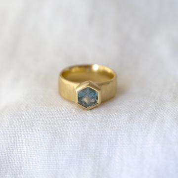 Set in a heavy 7mm 18K band this bold natural Montana sapphire springs to life with oceanic hues. The subtle organic texturing on the band combined with the geometric cut of the stone merge to create a lovely balance of modern and organic.