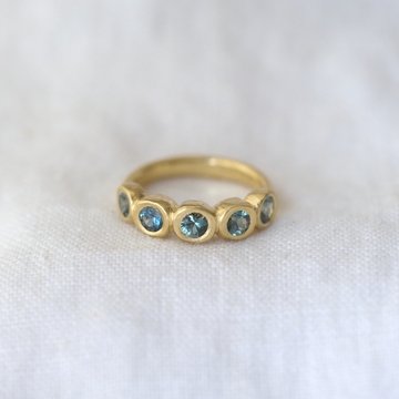 five teal montana sapphires bezel set in a row, with a thin gold band 