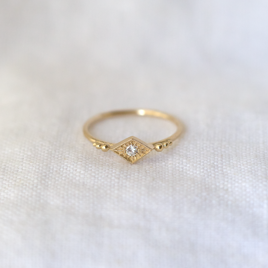 The diamond shape setting is flanked by 6 gold granules descending into a hammered textured band