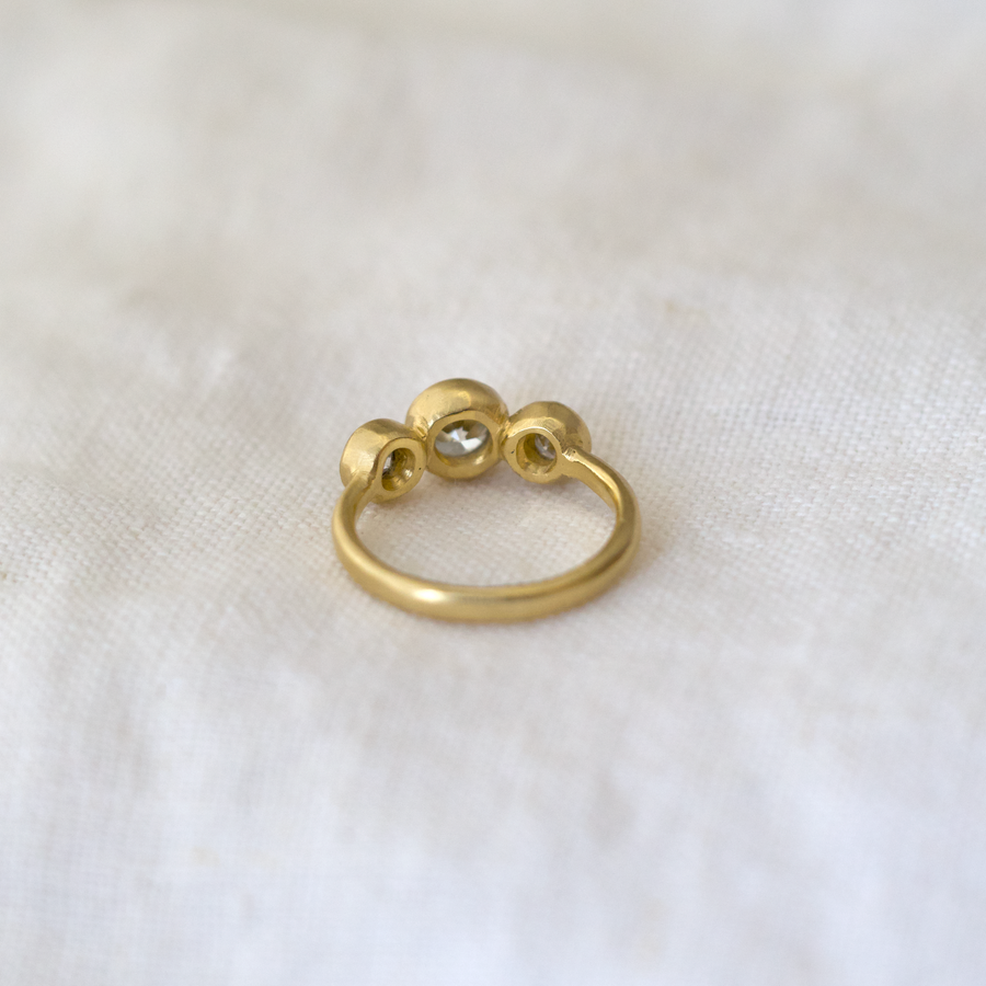 Gold ring with three circular elements on a white fabric background